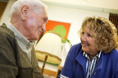 Eine Rotkreuzfreiwillige ist in ein Gespräch mit einem älteren Mann vertieft.